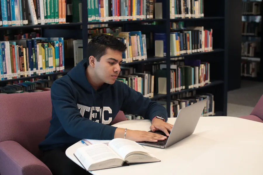 Man using a laptop beside an open book in a library