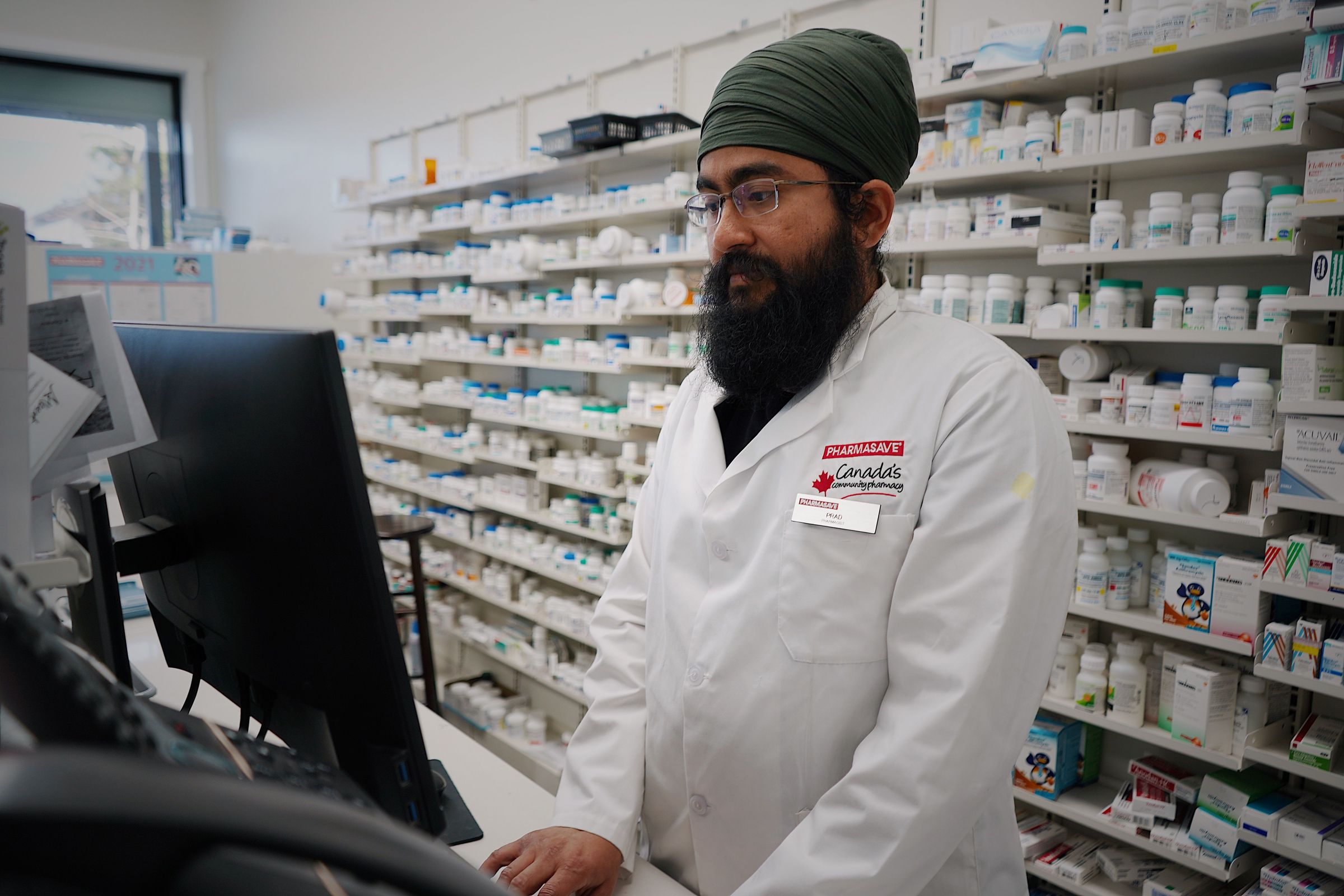 Pharmacist working at a computer beside medicine shelves