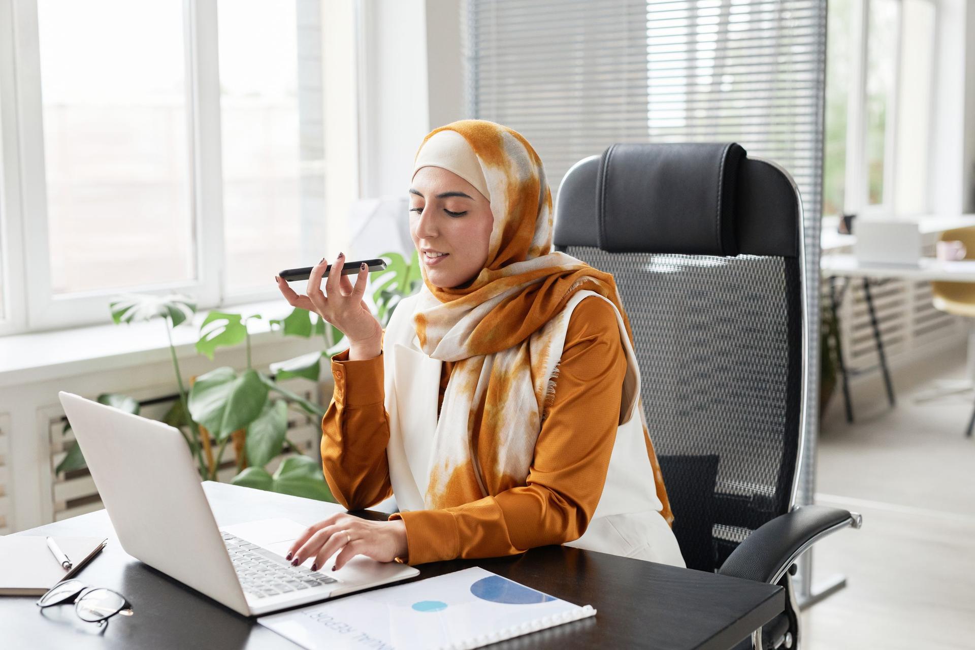 Arab customer service professional using AI support tools on a phone and laptop
