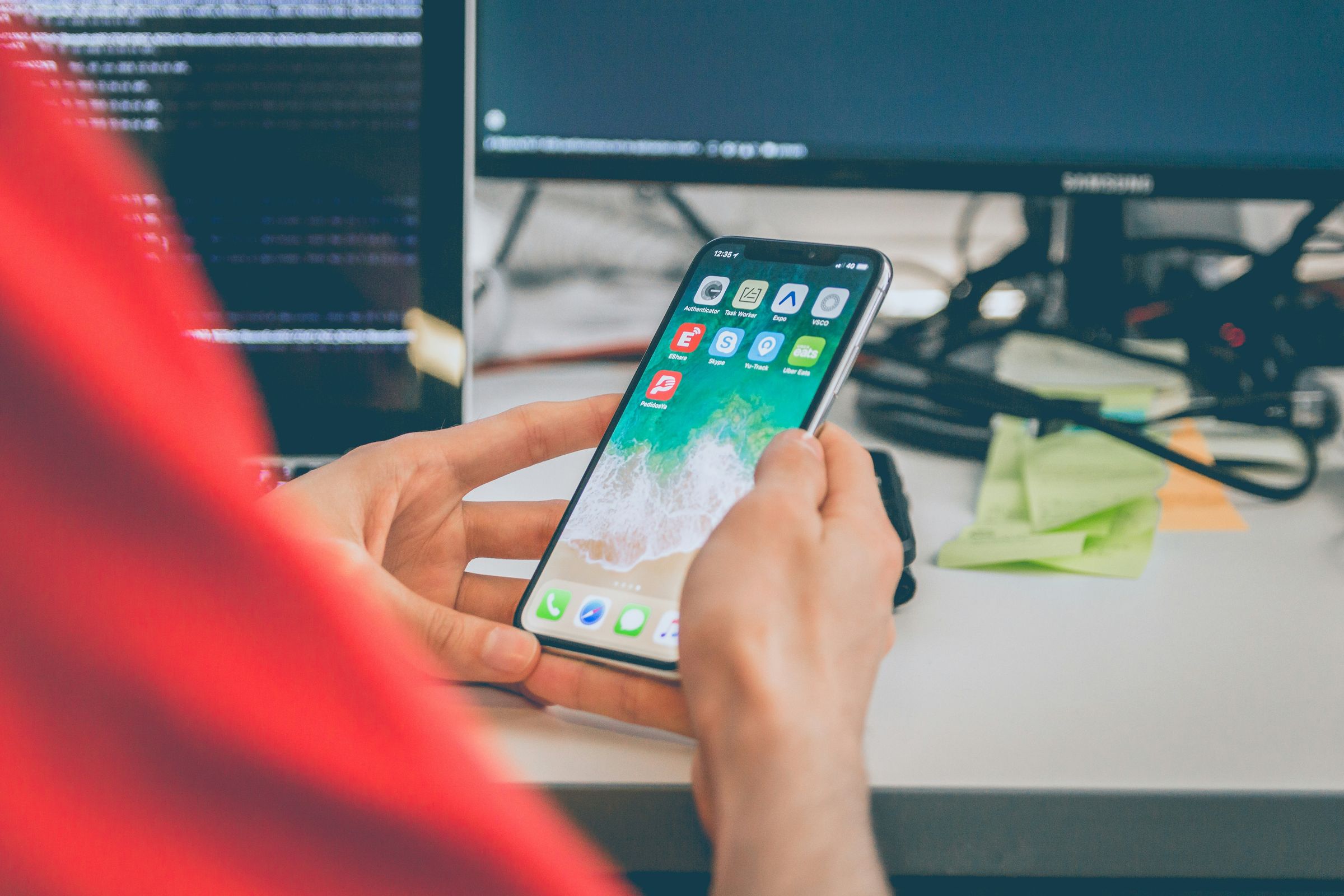 Person using a smartphone in front of screens showing software code