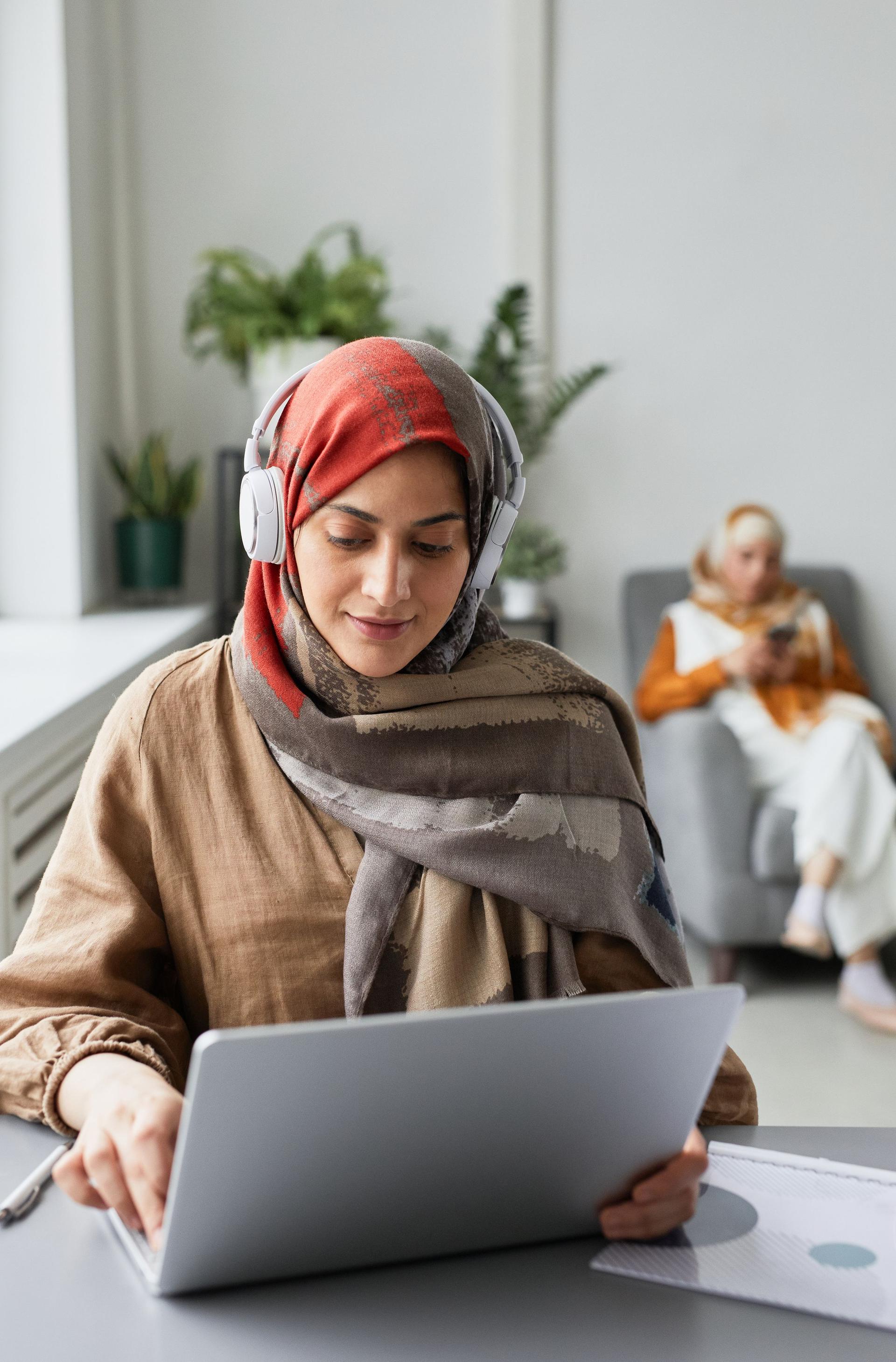 Arab woman in a headscarf using a laptop and headset in AI-assisted customer service