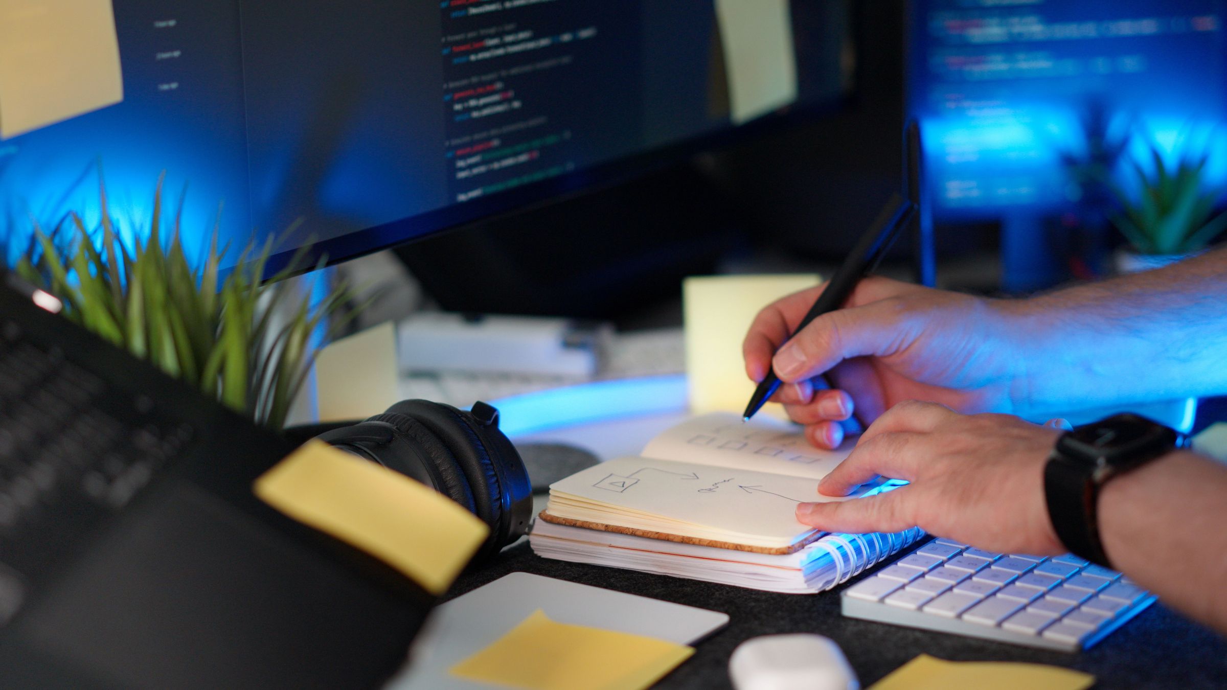 Hands writing notes beside a code screen and keyboard