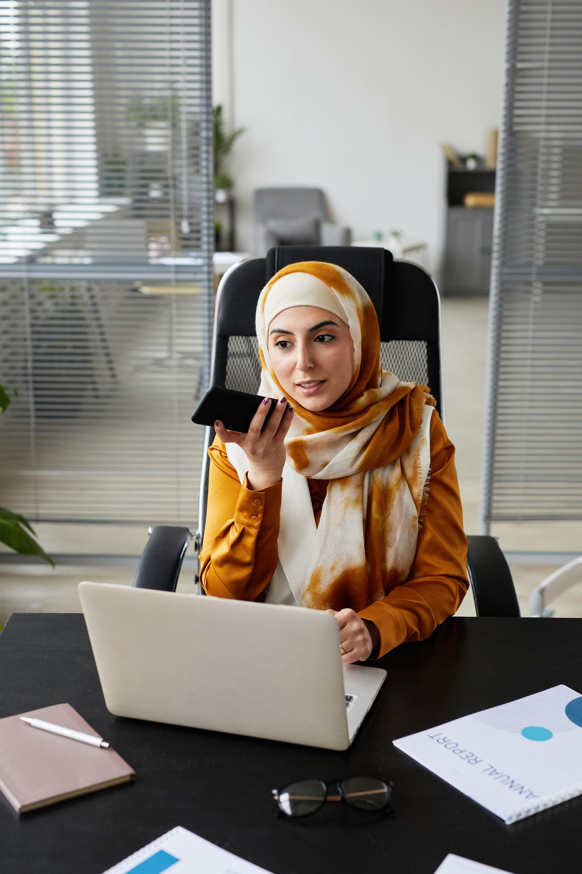 Arab businesswoman in a hijab using a laptop and phone to choose a software company in Saudi Arabia