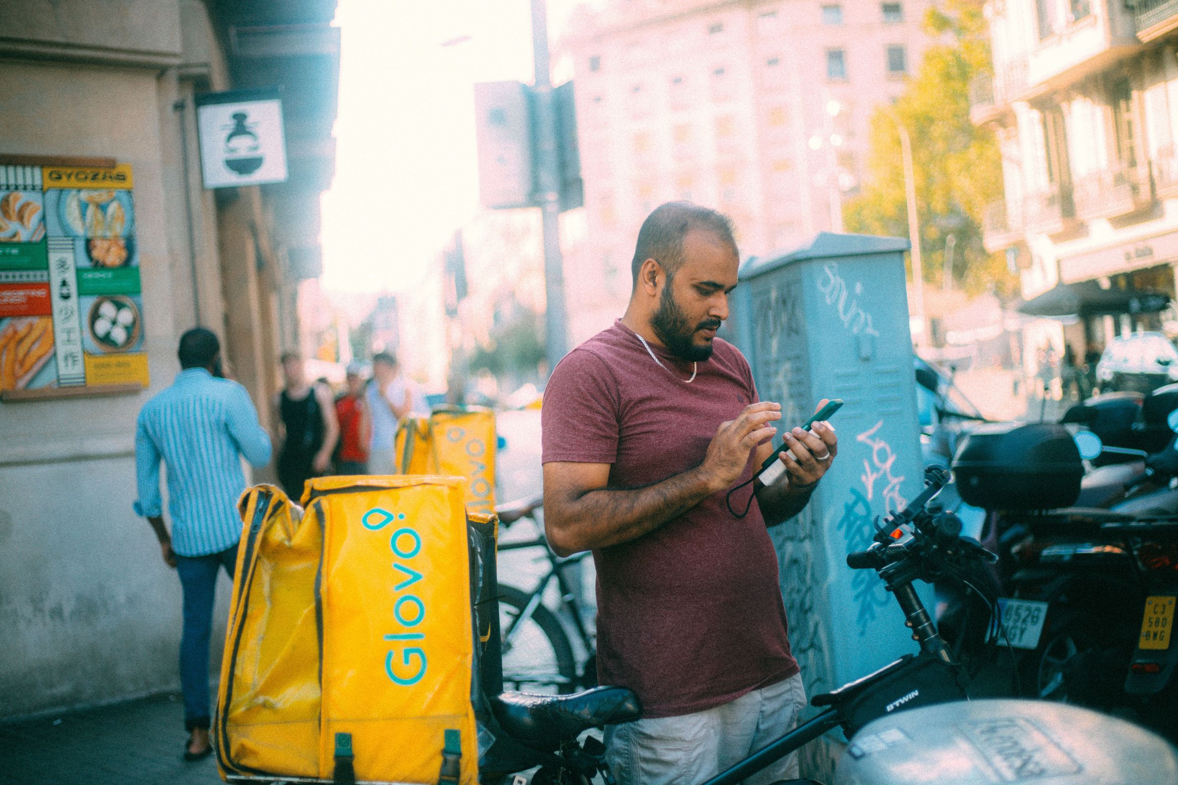 A courier uses a phone beside a bike and delivery bag