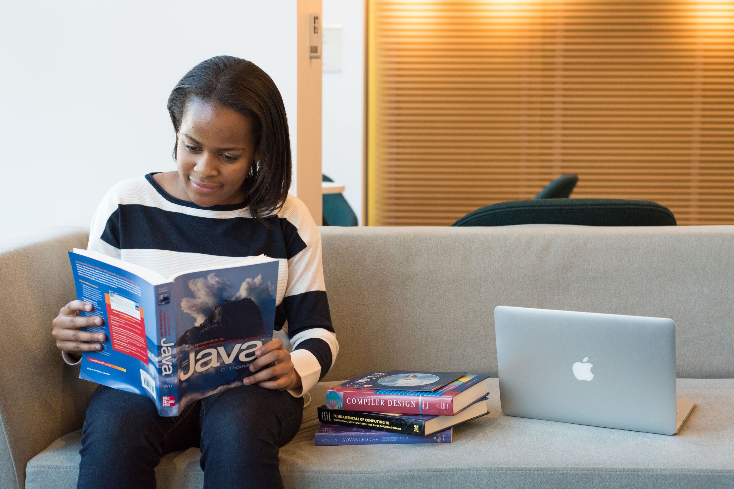 Woman reading a programming book beside other books and a laptop