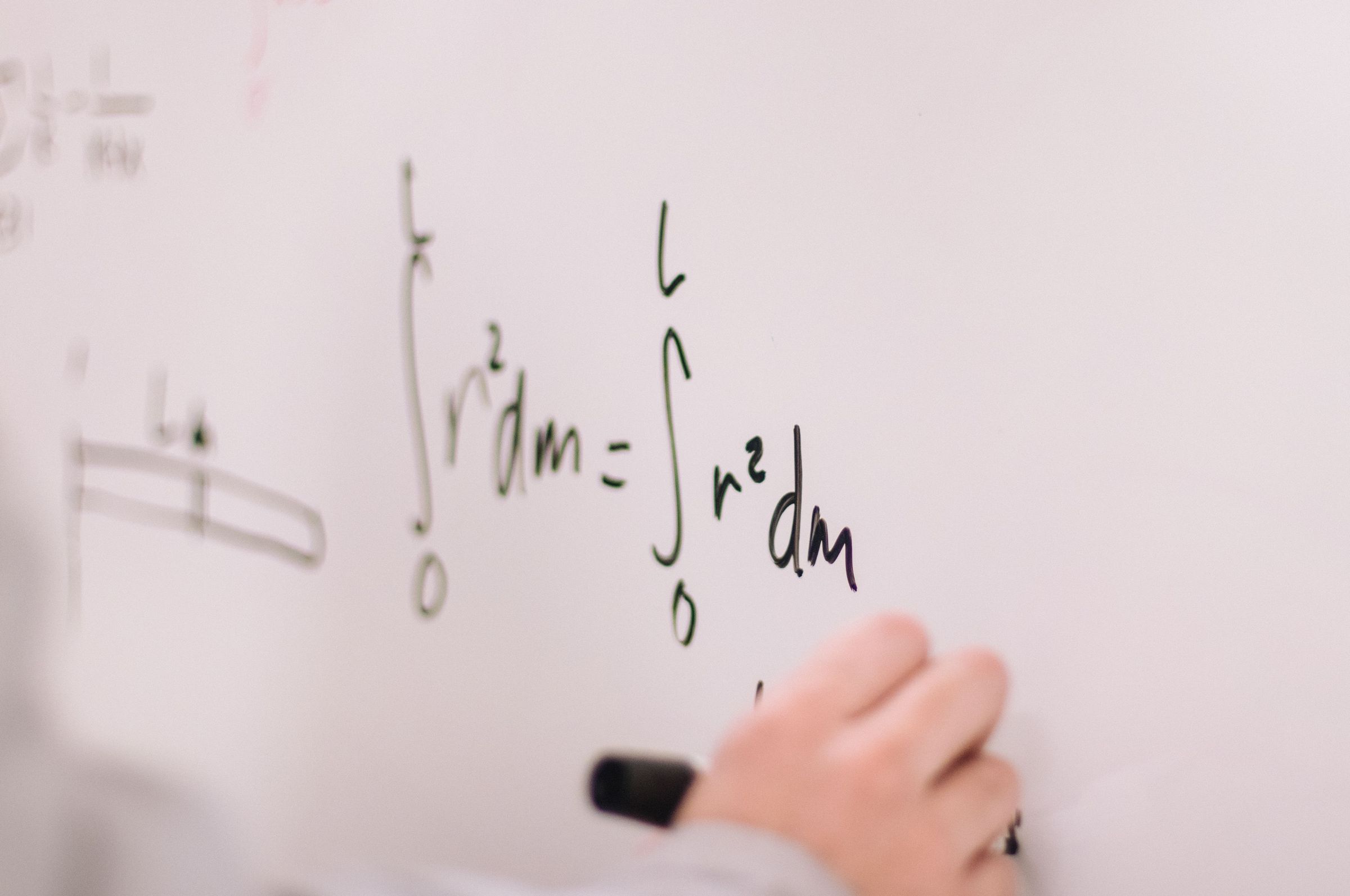 Person writing mathematical equations on a whiteboard