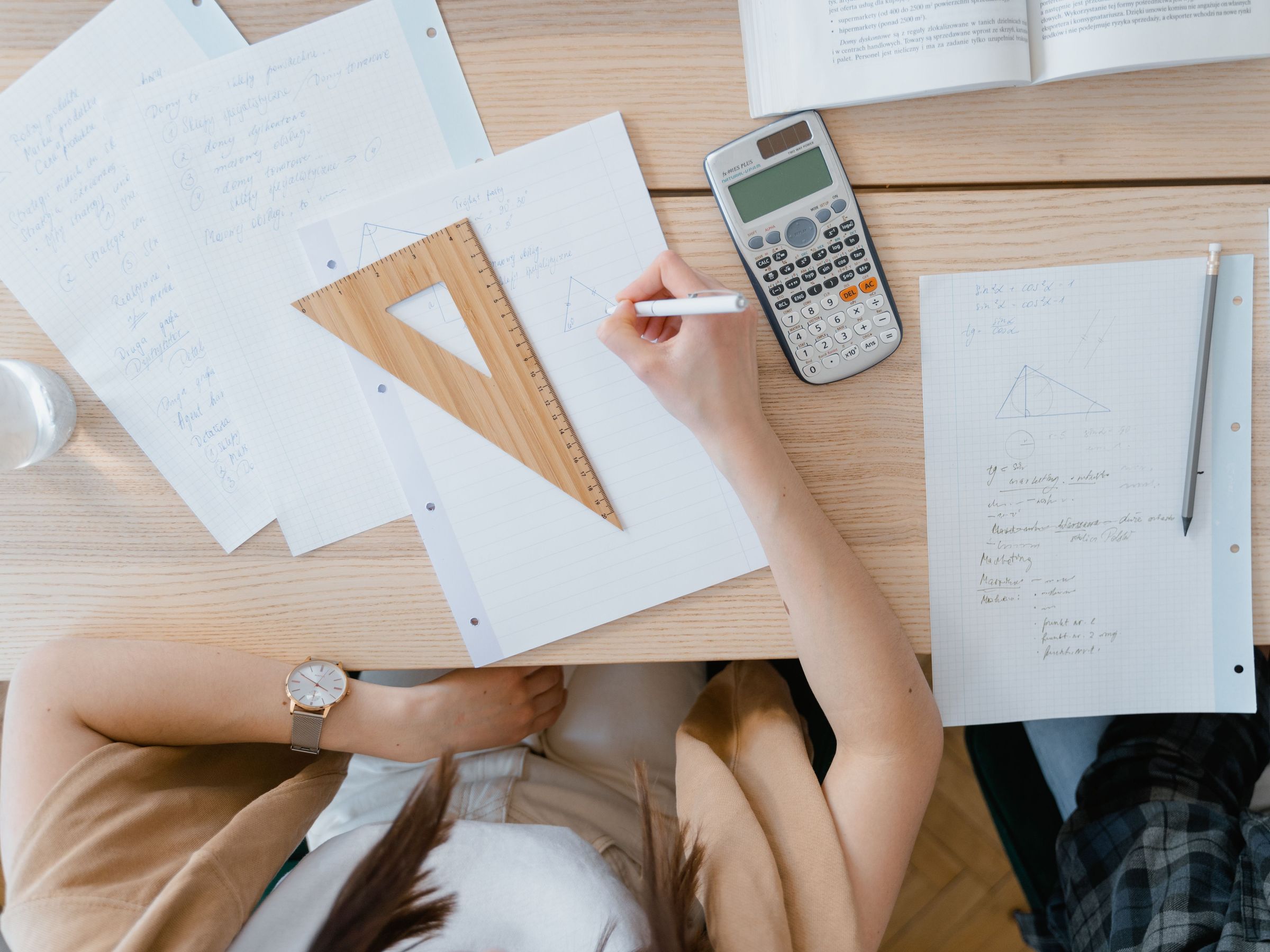 شخص يكتب ملاحظات هندسية بجانب آلة حاسبة وأدوات قياس