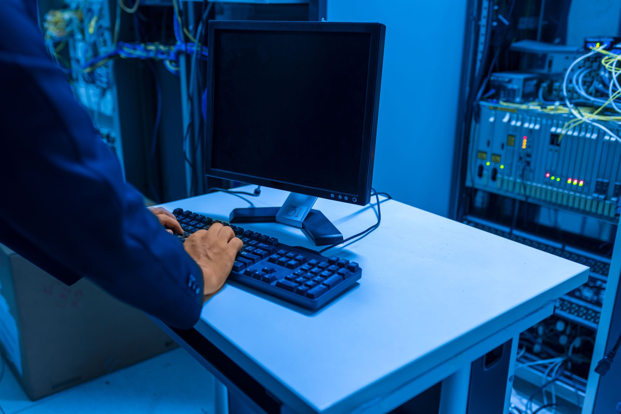 Technician using a keyboard beside server racks and a dark monitor