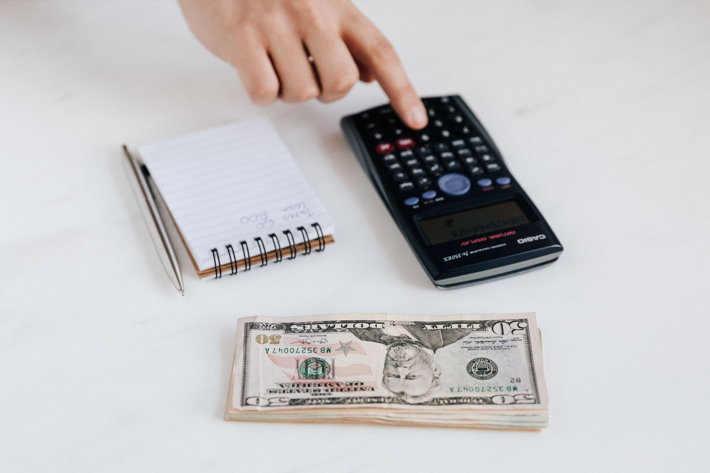 Hand using a calculator beside dollar notes and a notebook