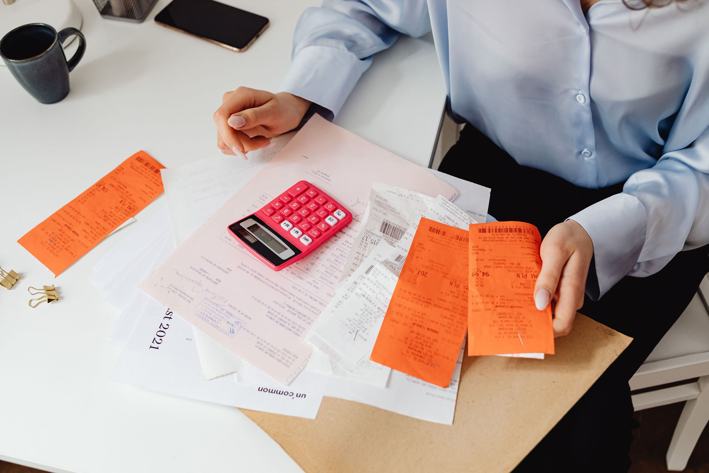 Person reviewing paper receipts beside a pink calculator