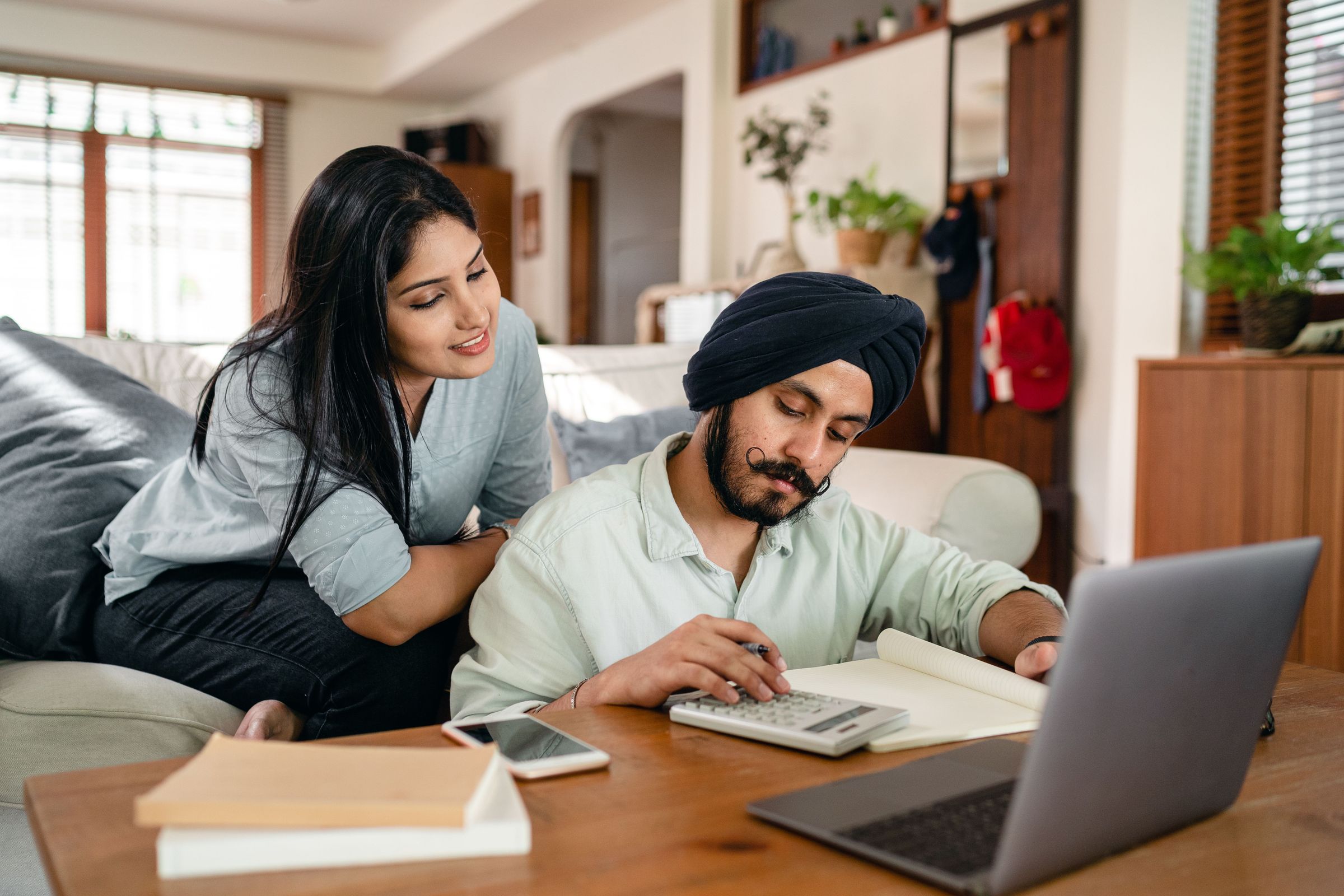 Man using a calculator and notebook beside a laptop while a woman observes