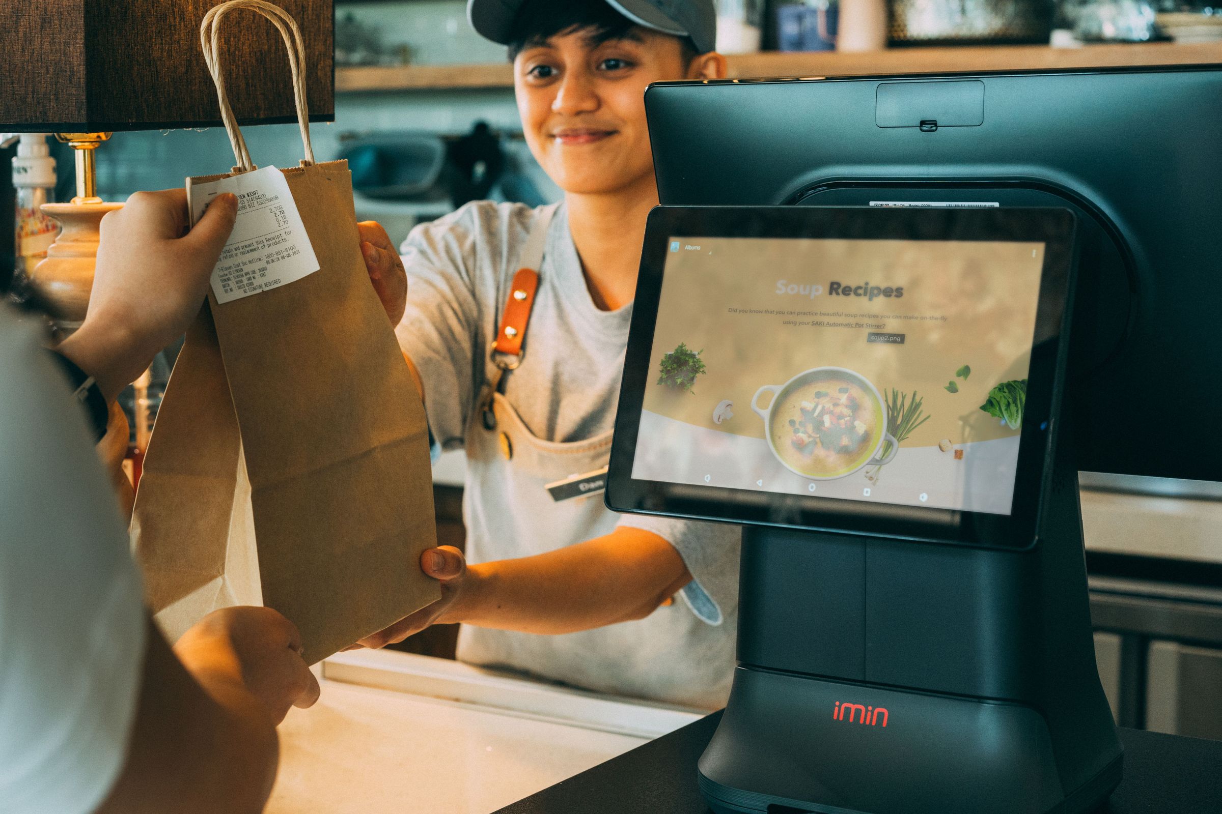 Worker handing a bag with a receipt to a customer beside a point of sale device