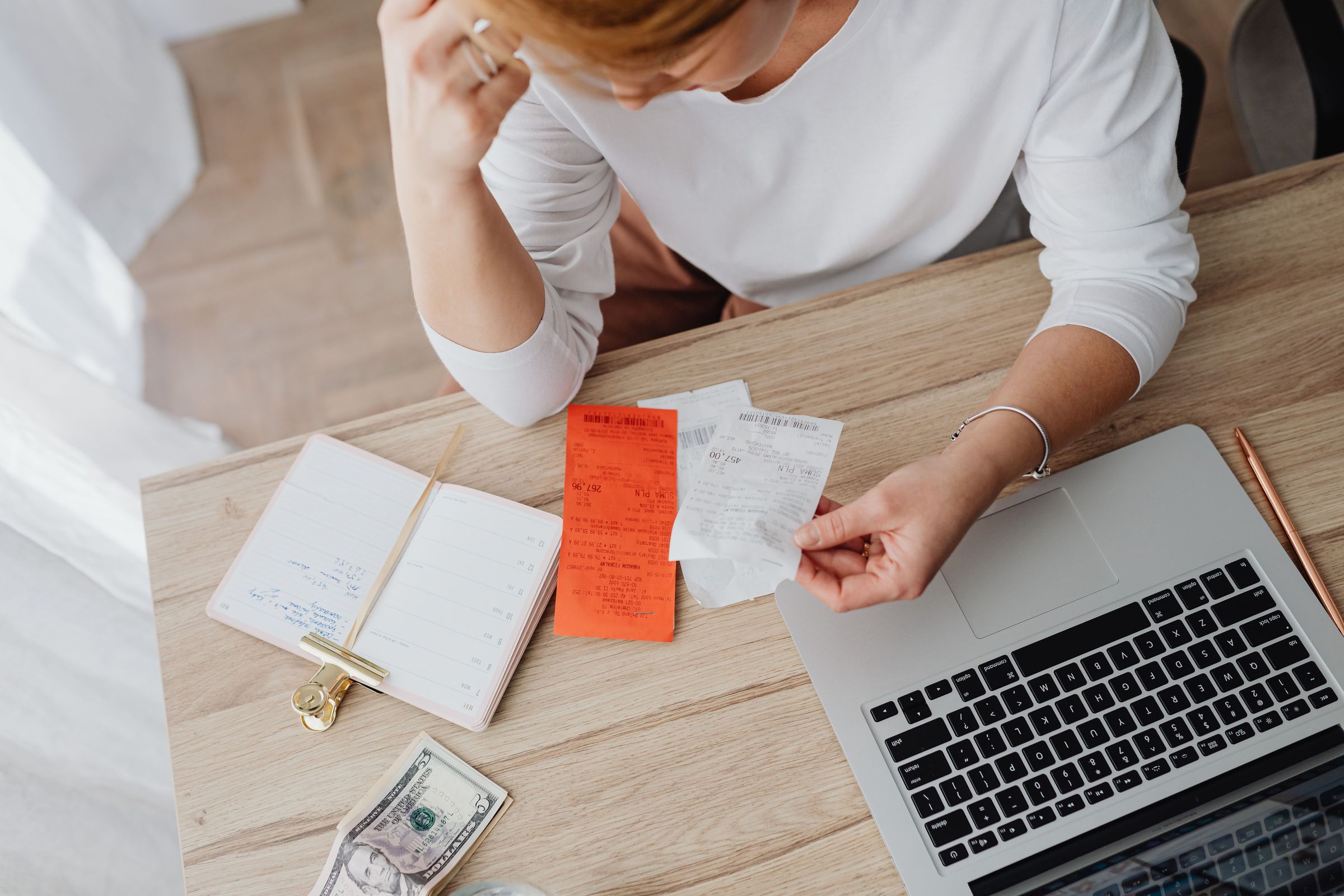 Person reviewing receipts beside a notebook and laptop