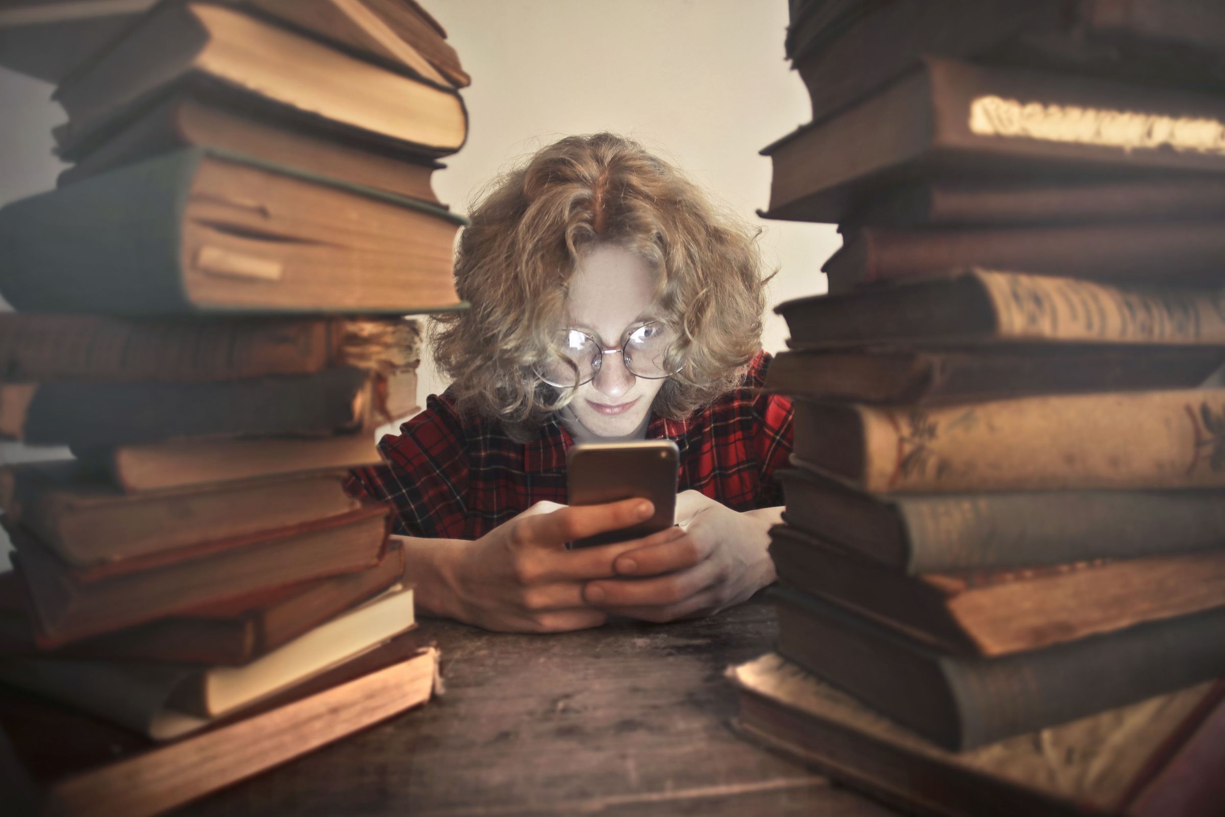 شخص بنظارة يستخدم هاتفاً بين أكوام كتب على طاولة