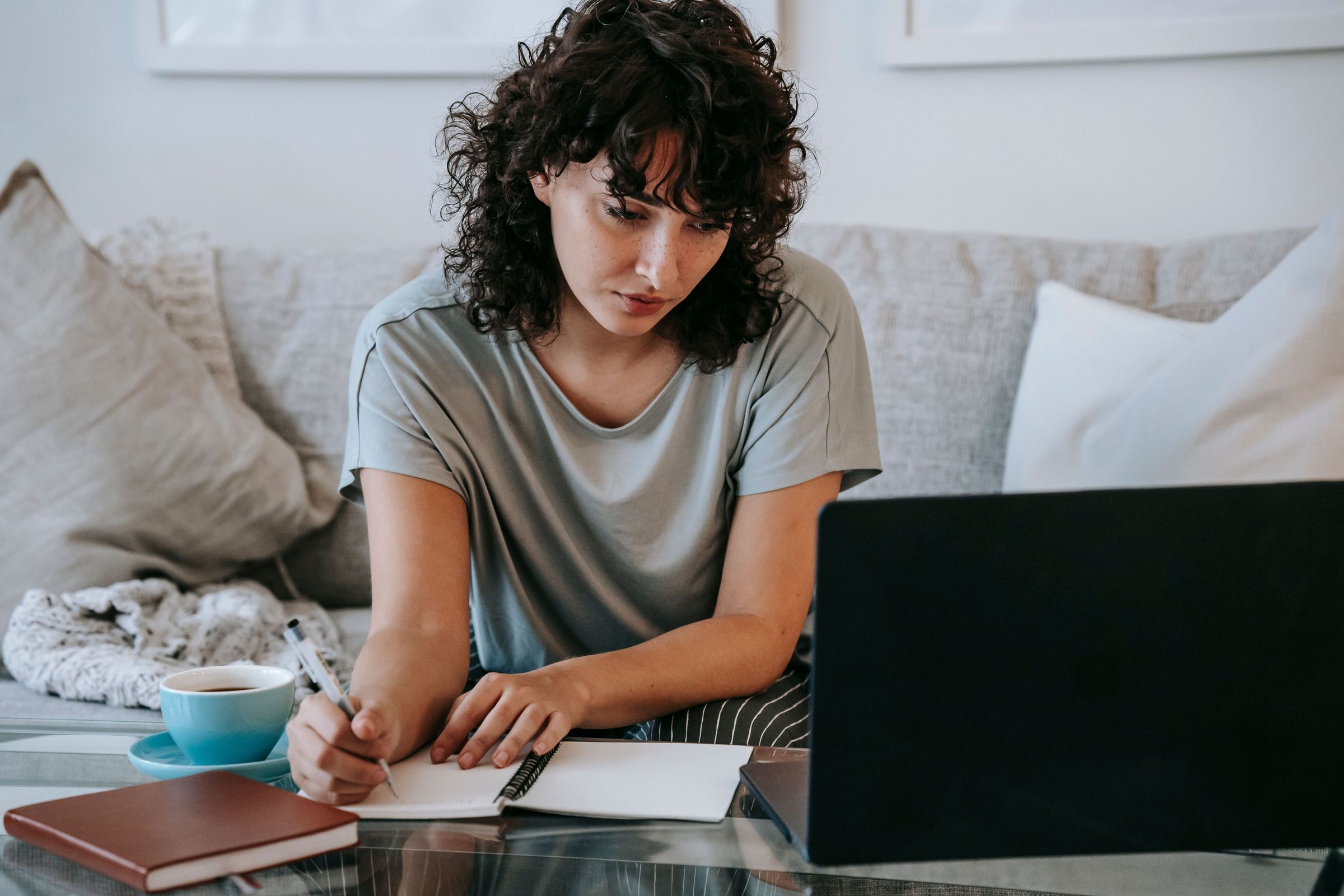 Woman taking notes beside a laptop in front of a sofa