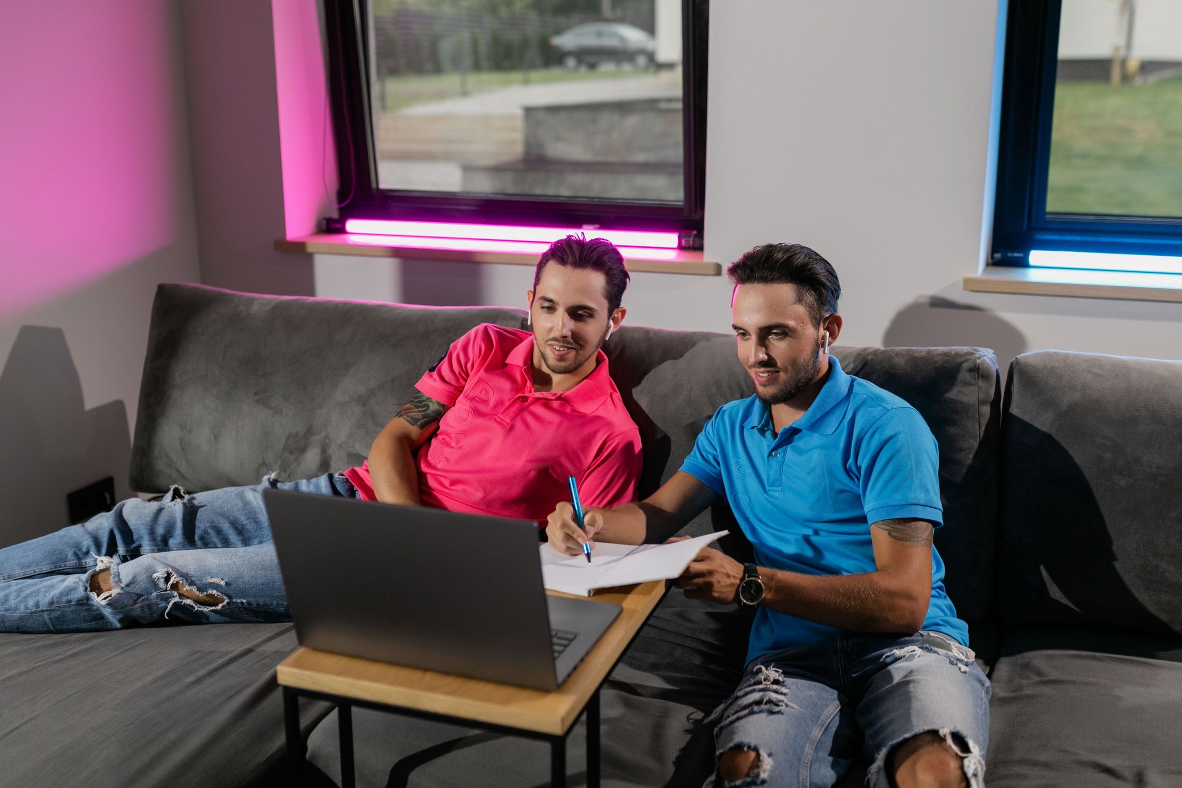 Two men reviewing a laptop with a notebook on a sofa