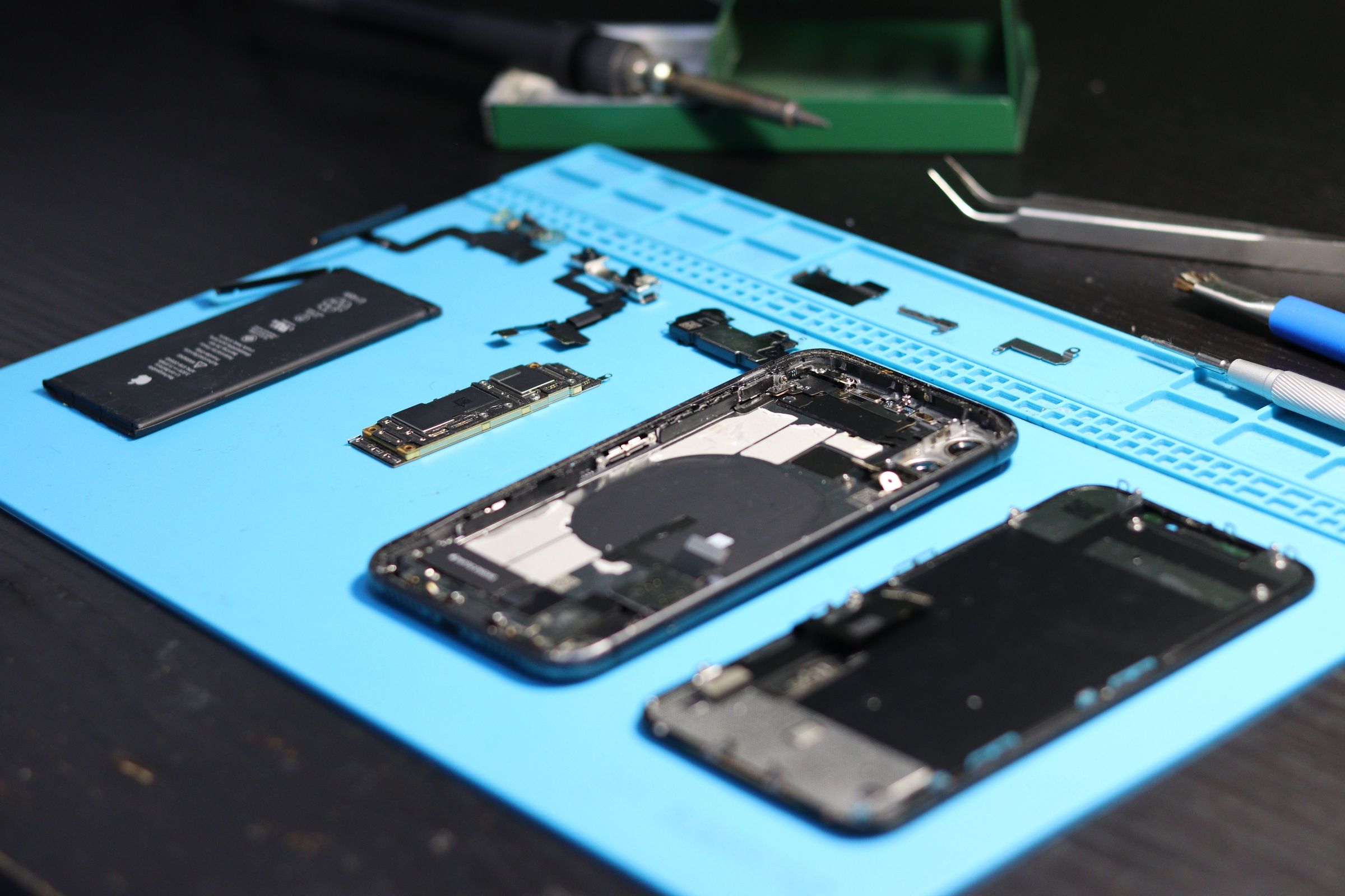 Disassembled phone and components with precision tools on a blue repair mat