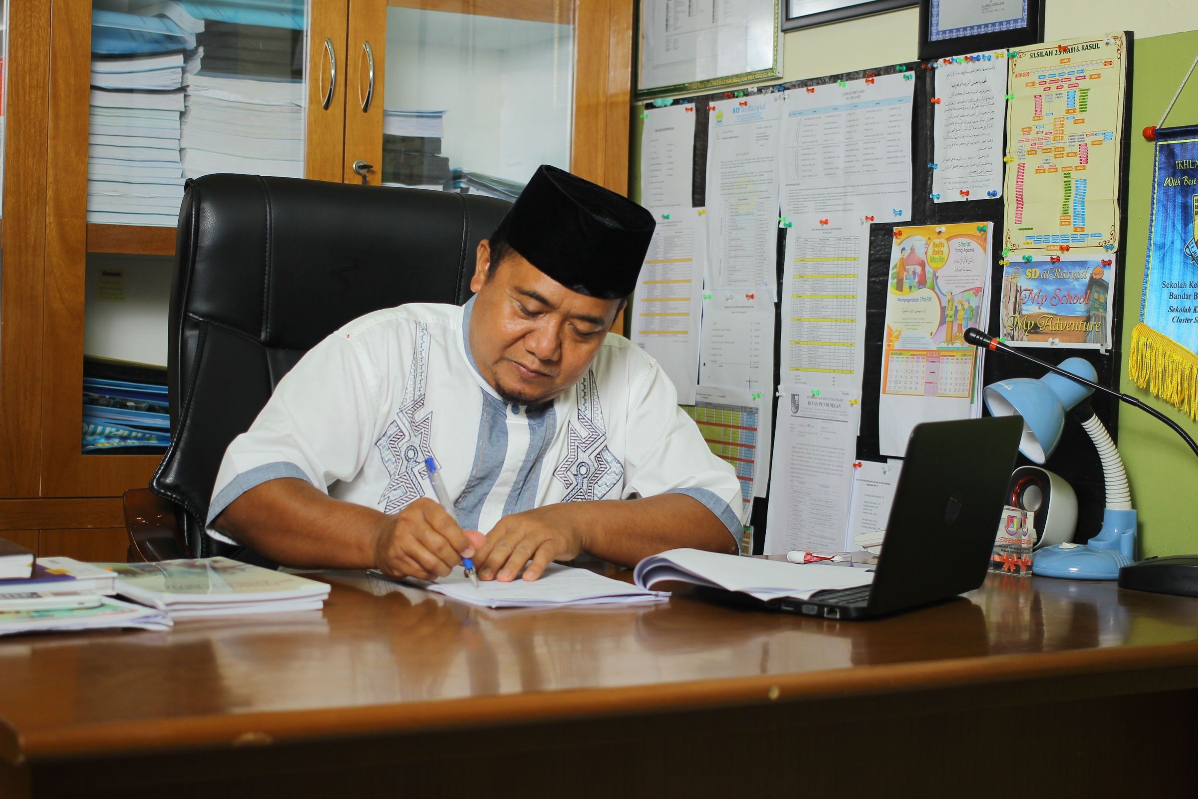 School principal writing on documents at his office desk in Indonesia