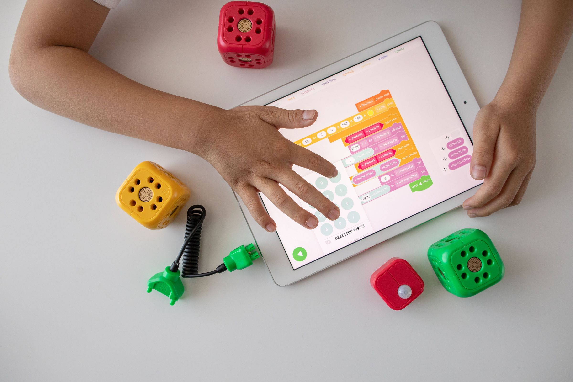 Child hands using a tablet displaying coding blocks beside educational cubes