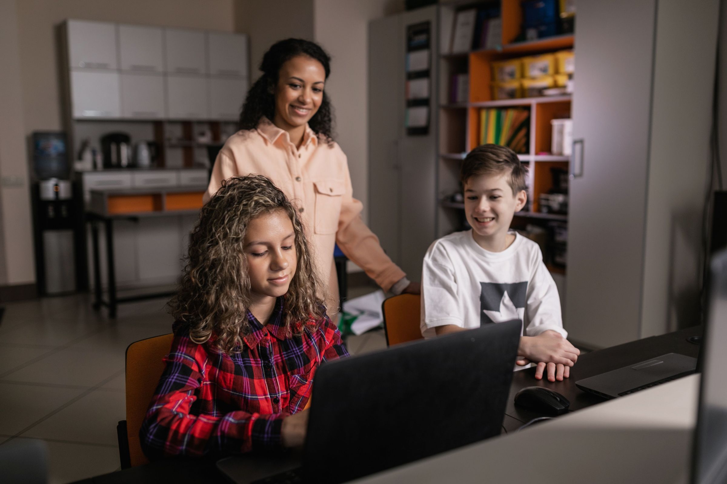 Two children at laptops with adult supervision in a general licensed photograph