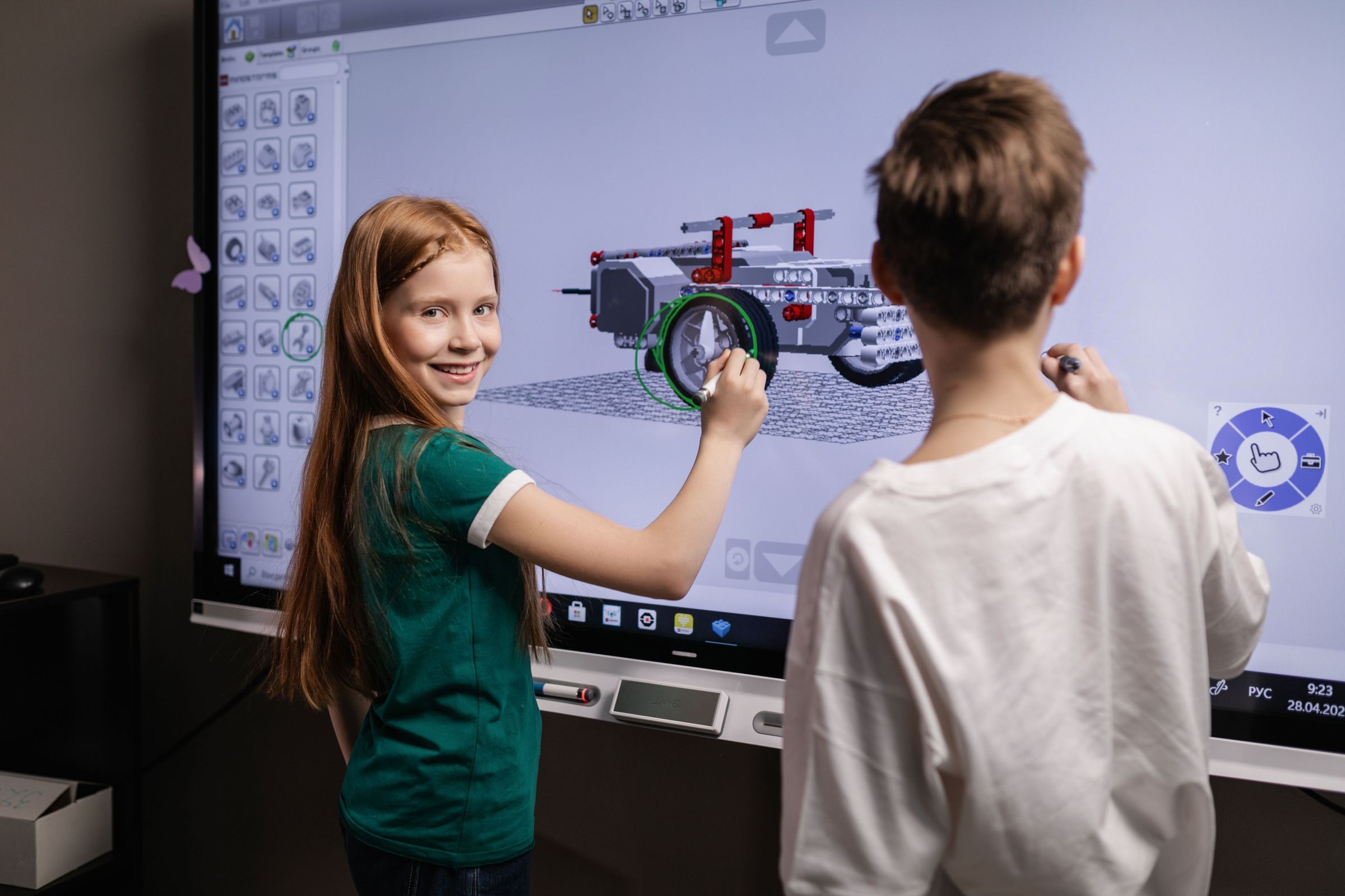 Two children interacting with a three dimensional vehicle model on a classroom screen in a real photograph