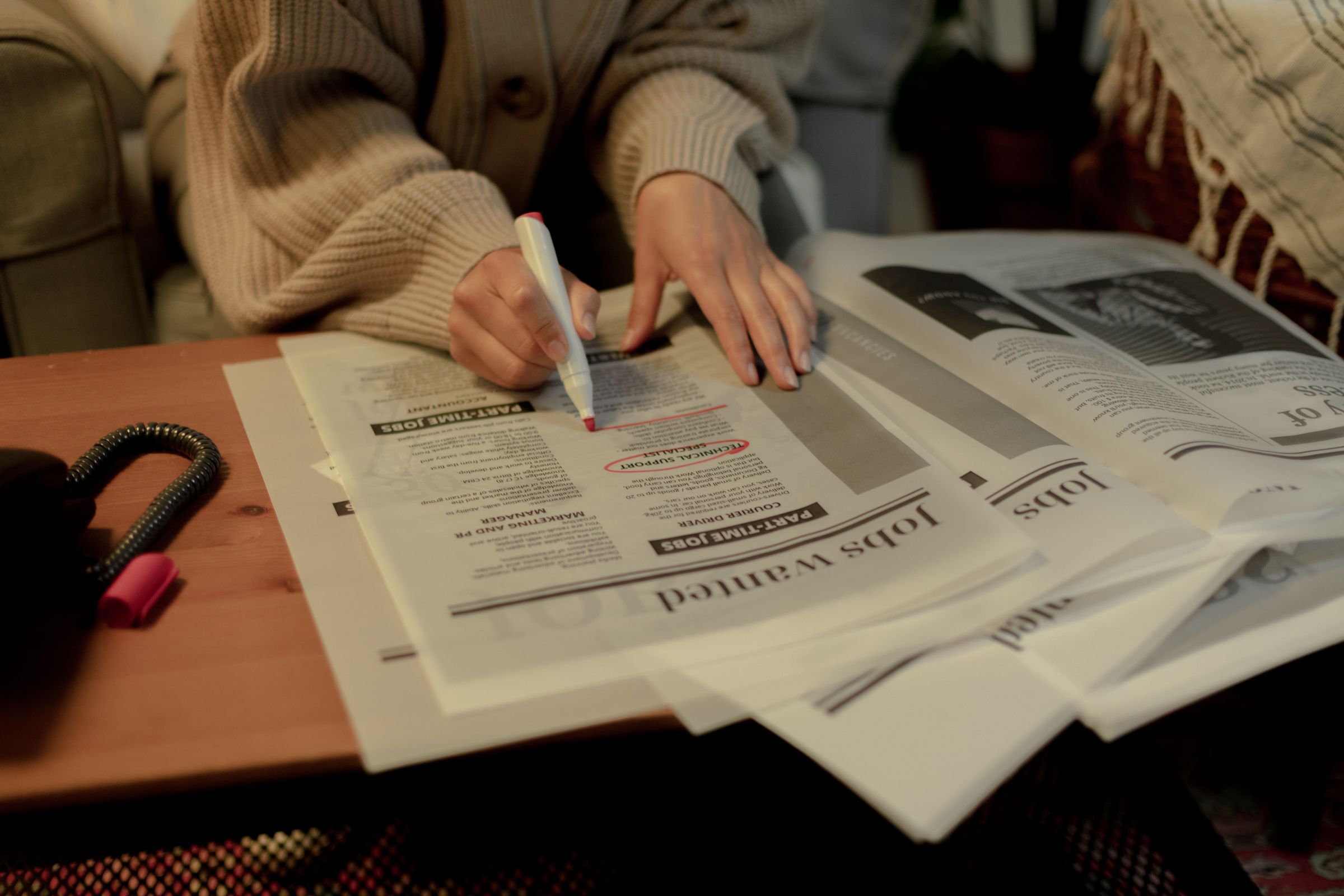 Person reviewing printed job advertisements and marking them with a pen