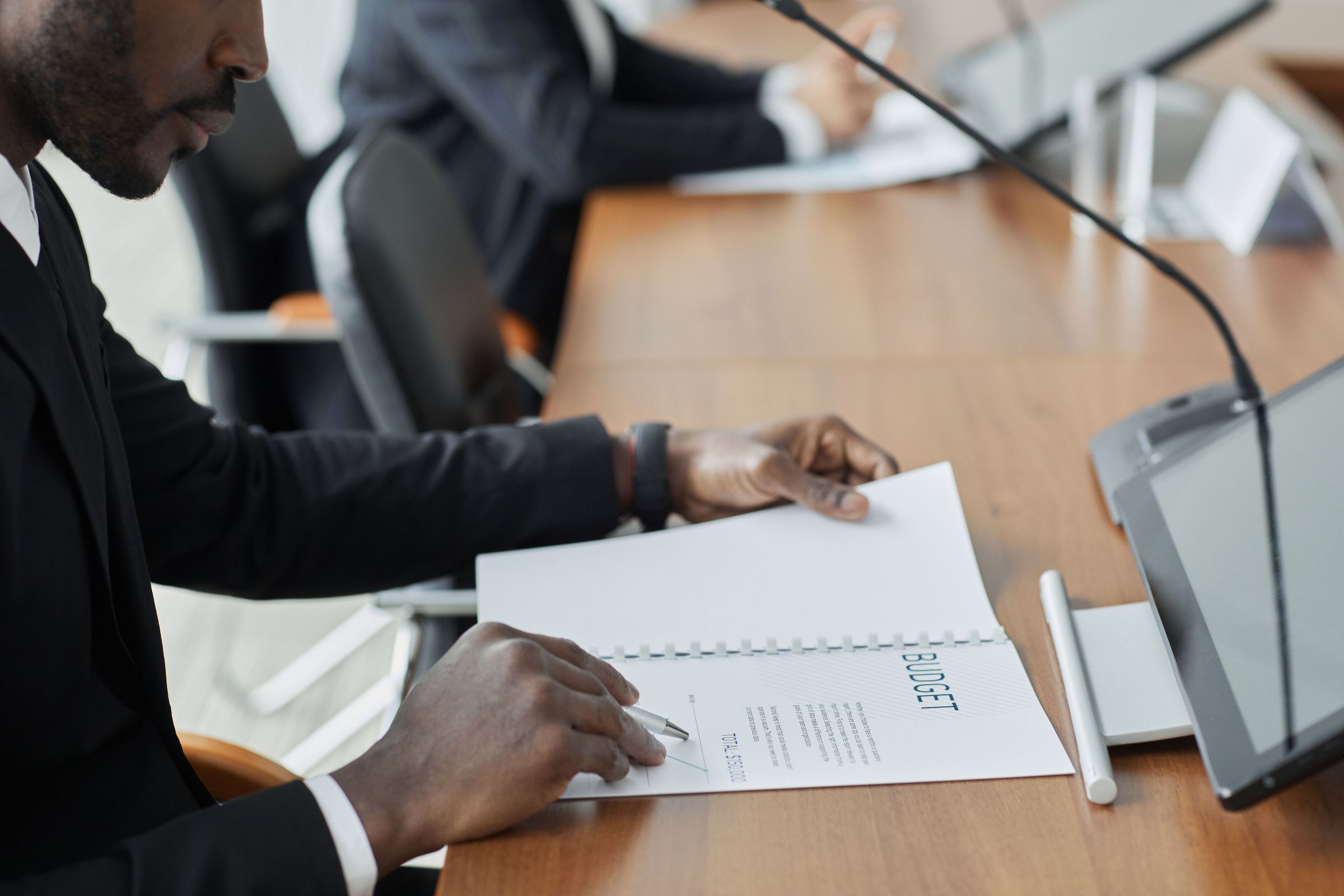 Man reviewing a budget document with a pen beside a laptop during a meeting