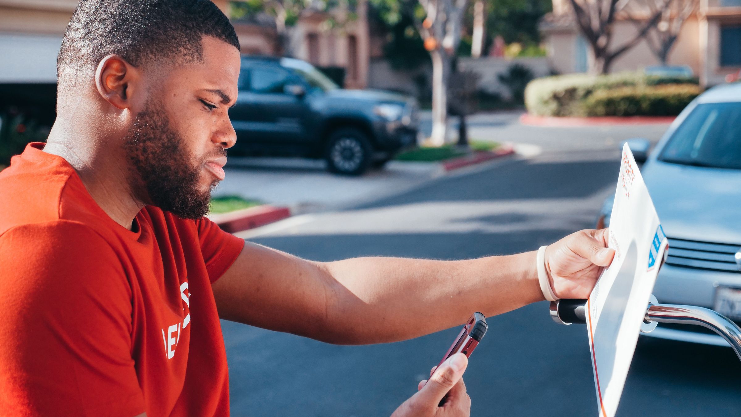 Courier carrying a parcel and looking at his phone outdoors