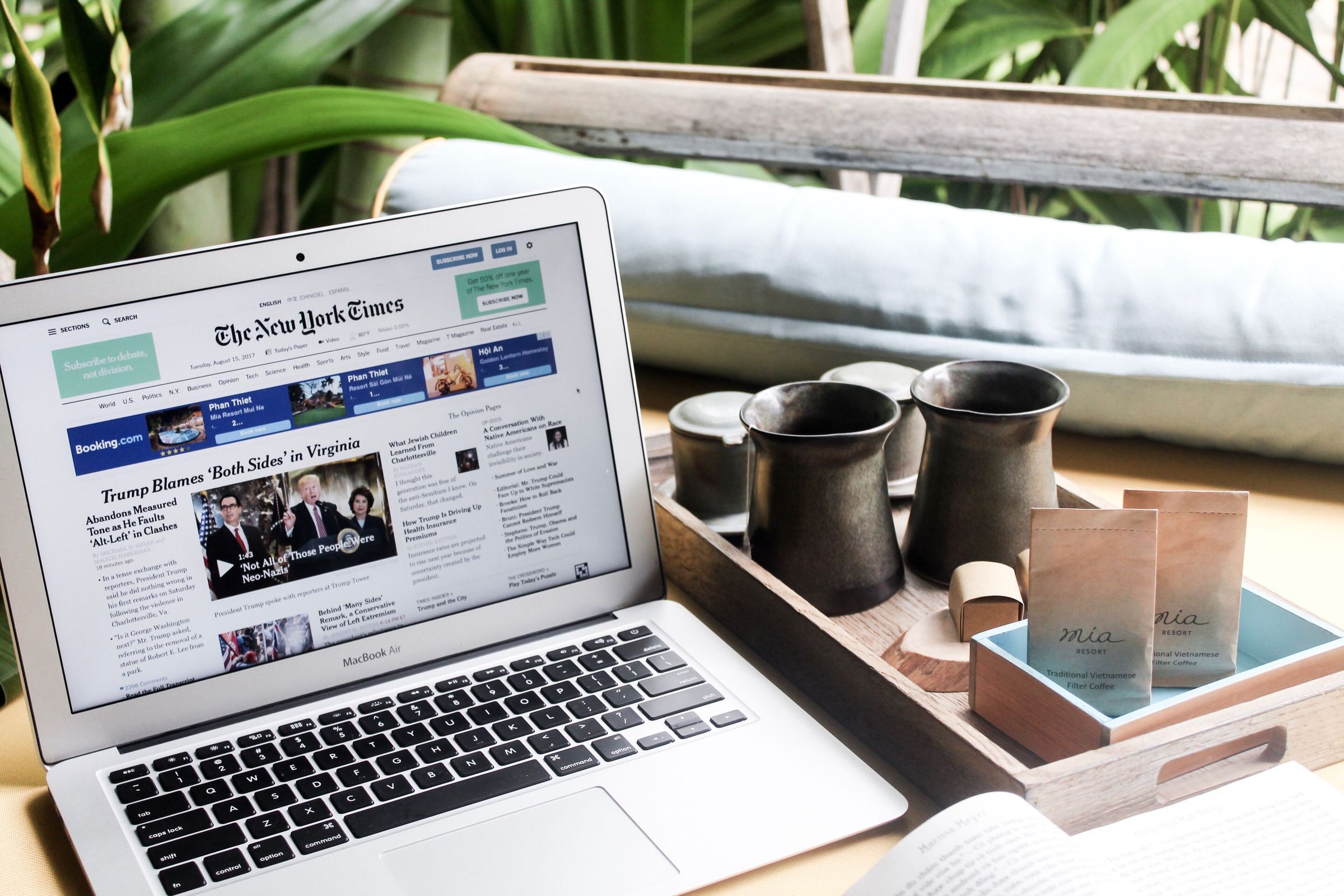 Laptop displaying a news website beside a tray and cups