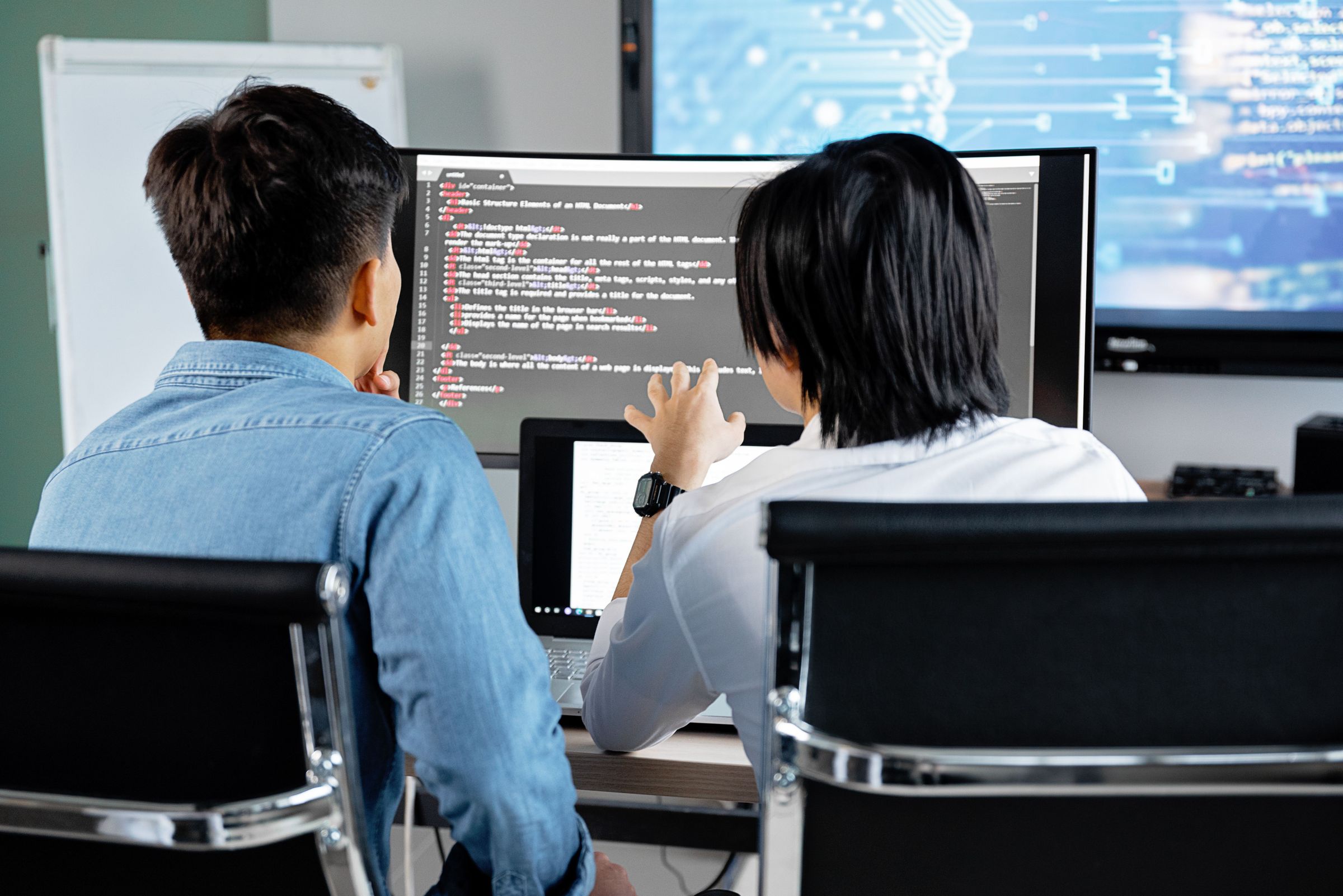 Back view of two people discussing code on a large monitor