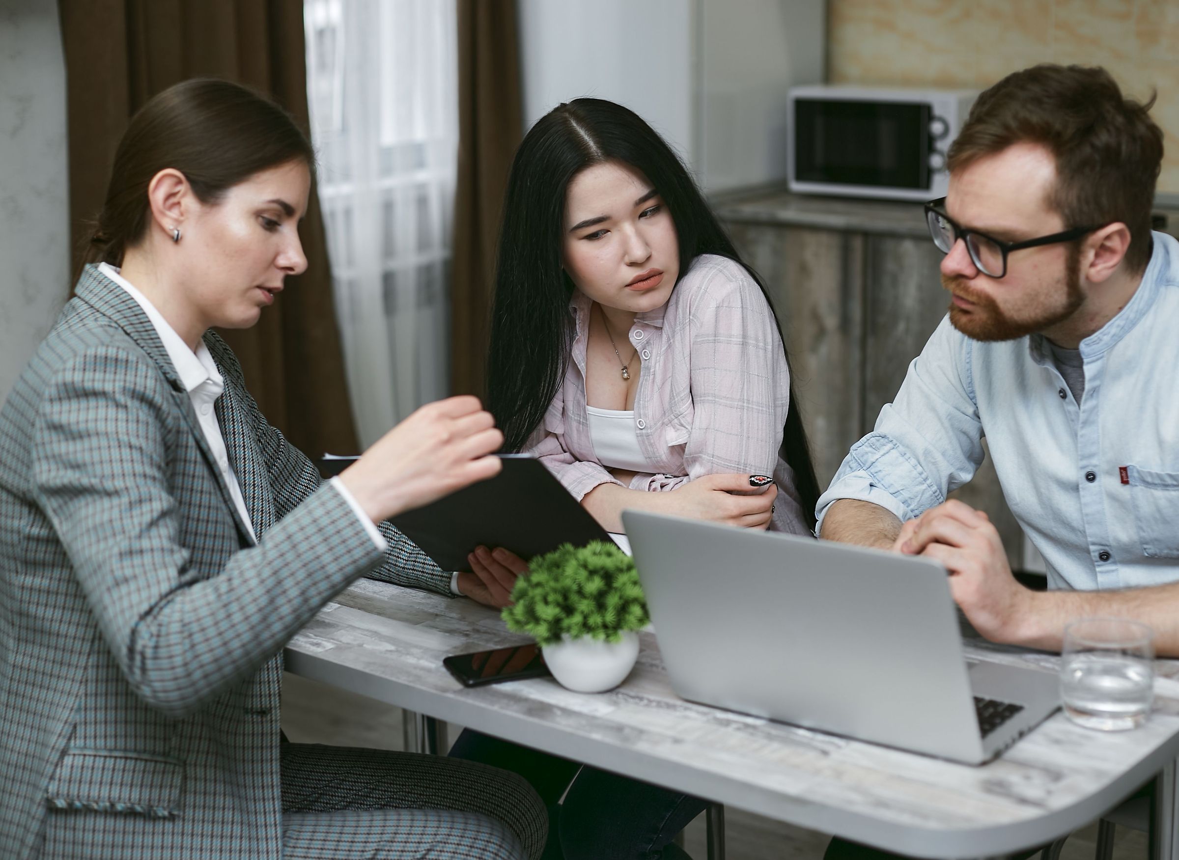 Three people discussing a folder beside a laptop