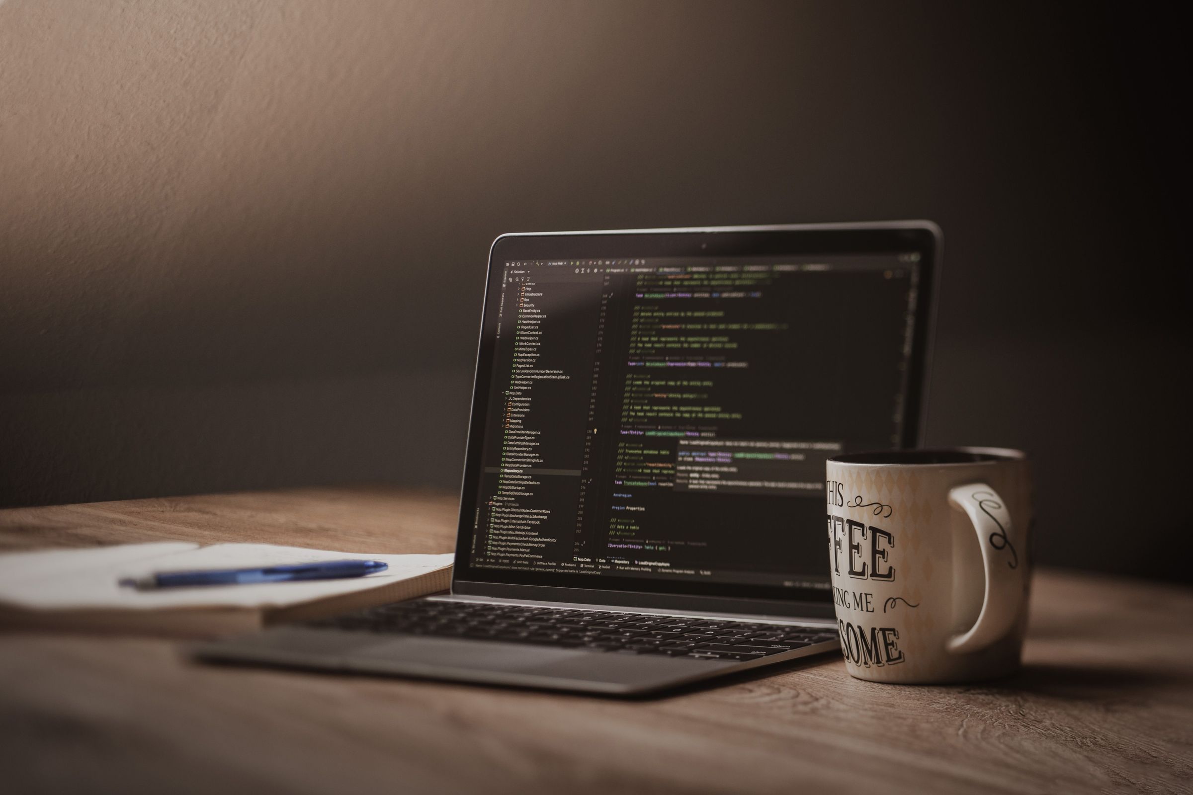 Code screen beside a notebook, pen and mug on a desk