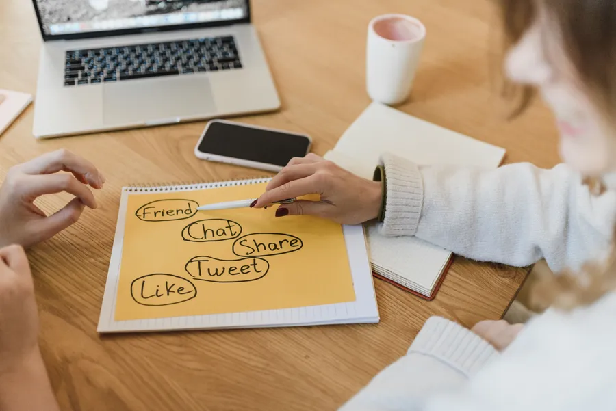 Planning social media content ideas on a notebook beside a laptop