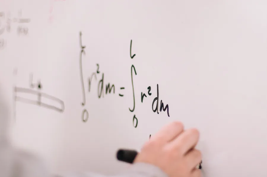Person writing mathematical equations on a whiteboard